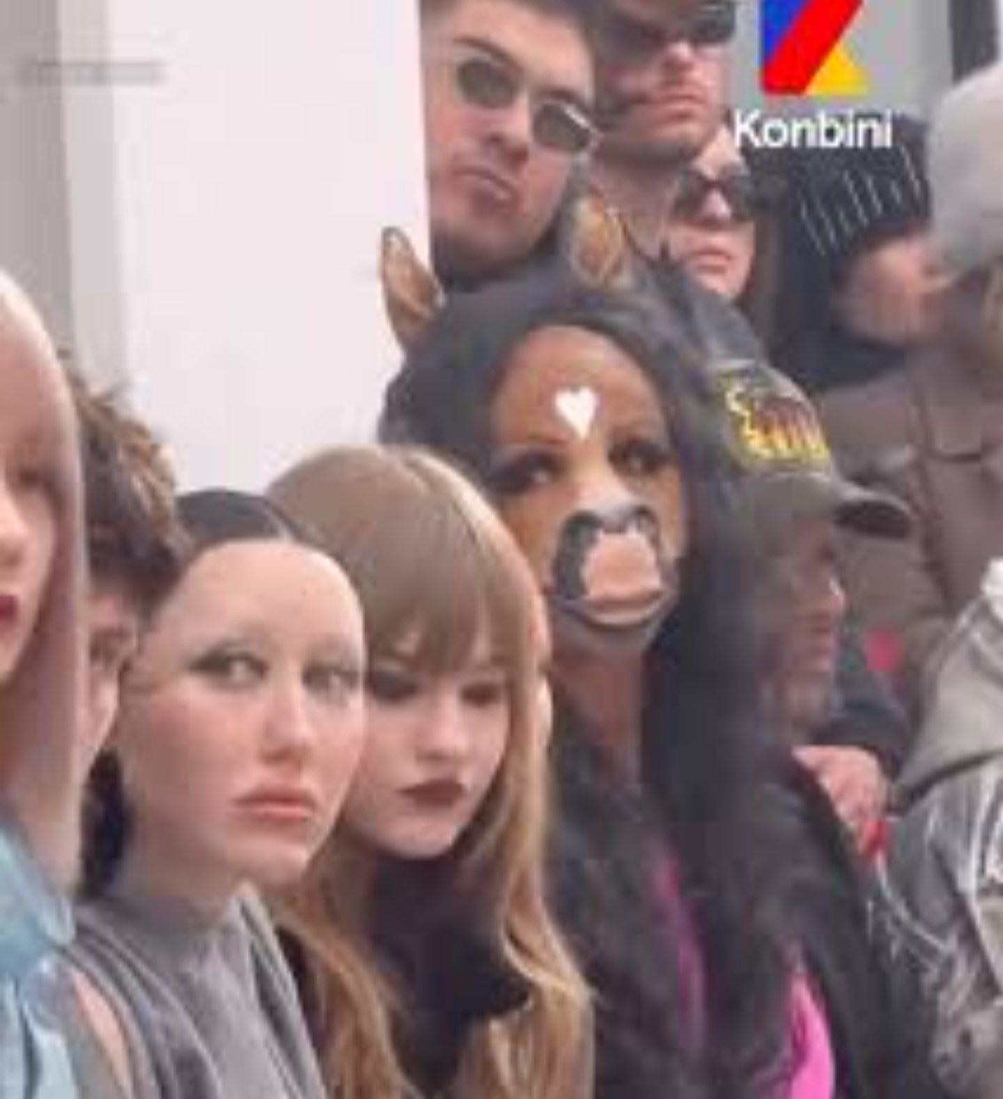 A crowd of similarly styled fashion-show attendees, one of them wearing a horse mask